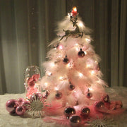 Small pink feather Christmas tree decorated with LED lights and pink Christmas ornaments on a tabletop