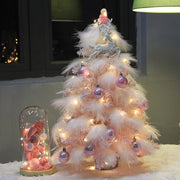 Small pink feather Christmas tree with LED lights and purple Christmas ornaments on a desktop decoration