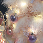 Close-up of small pink feather Christmas tree decorated with purple Christmas ornament balls and warm LED lights